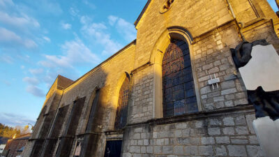 Façade de l’église Saint-Hubert de Redu avec vitraux et sculpture contemporaine au premier plan (Space Art Gallery)