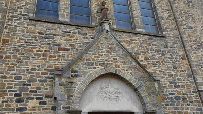 Façade en pierre de l’église Saint-François à Bastogne avec porte d’entrée et vitraux